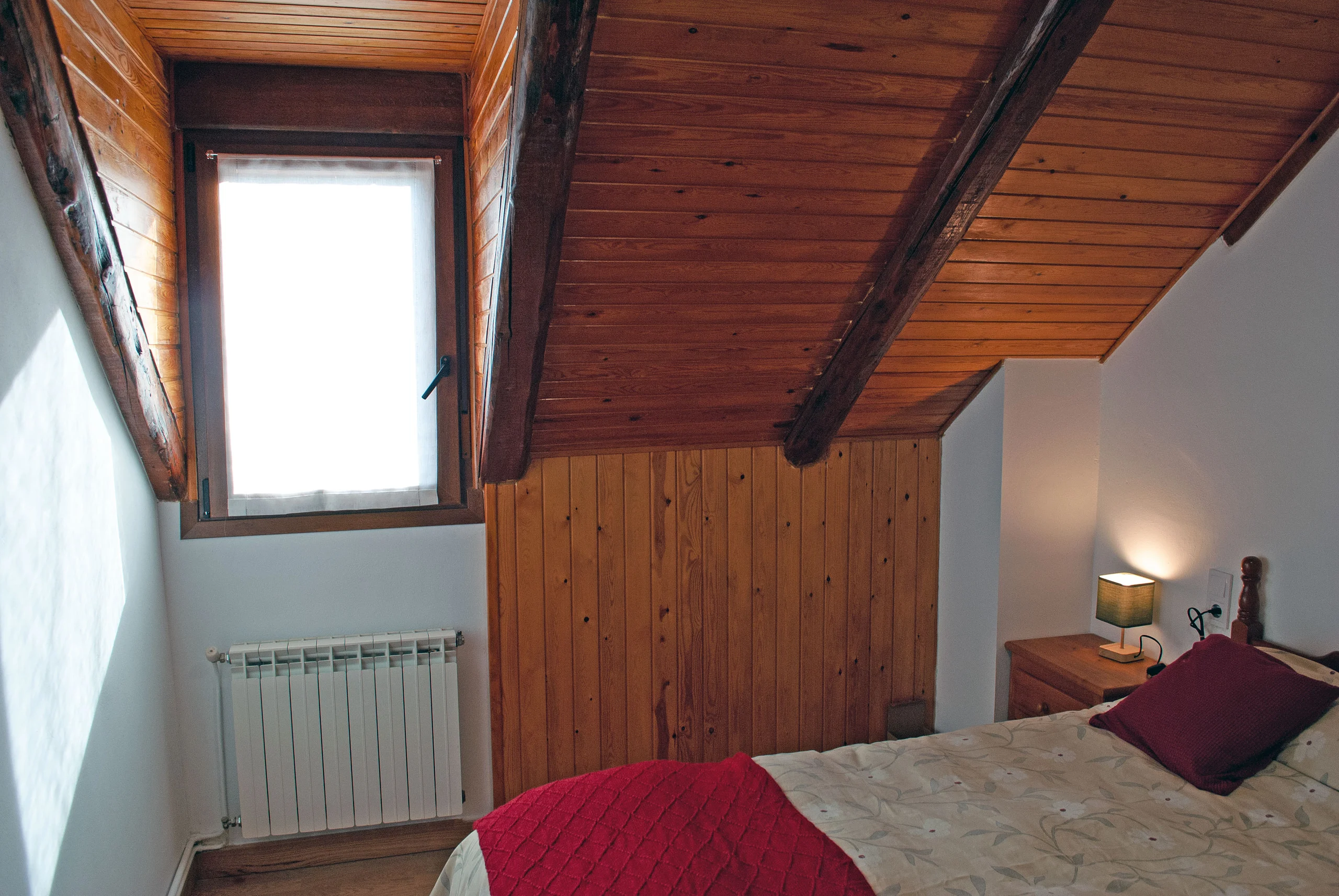 Dormitorio bajo las vigas de madera, con la pared forrada de madera