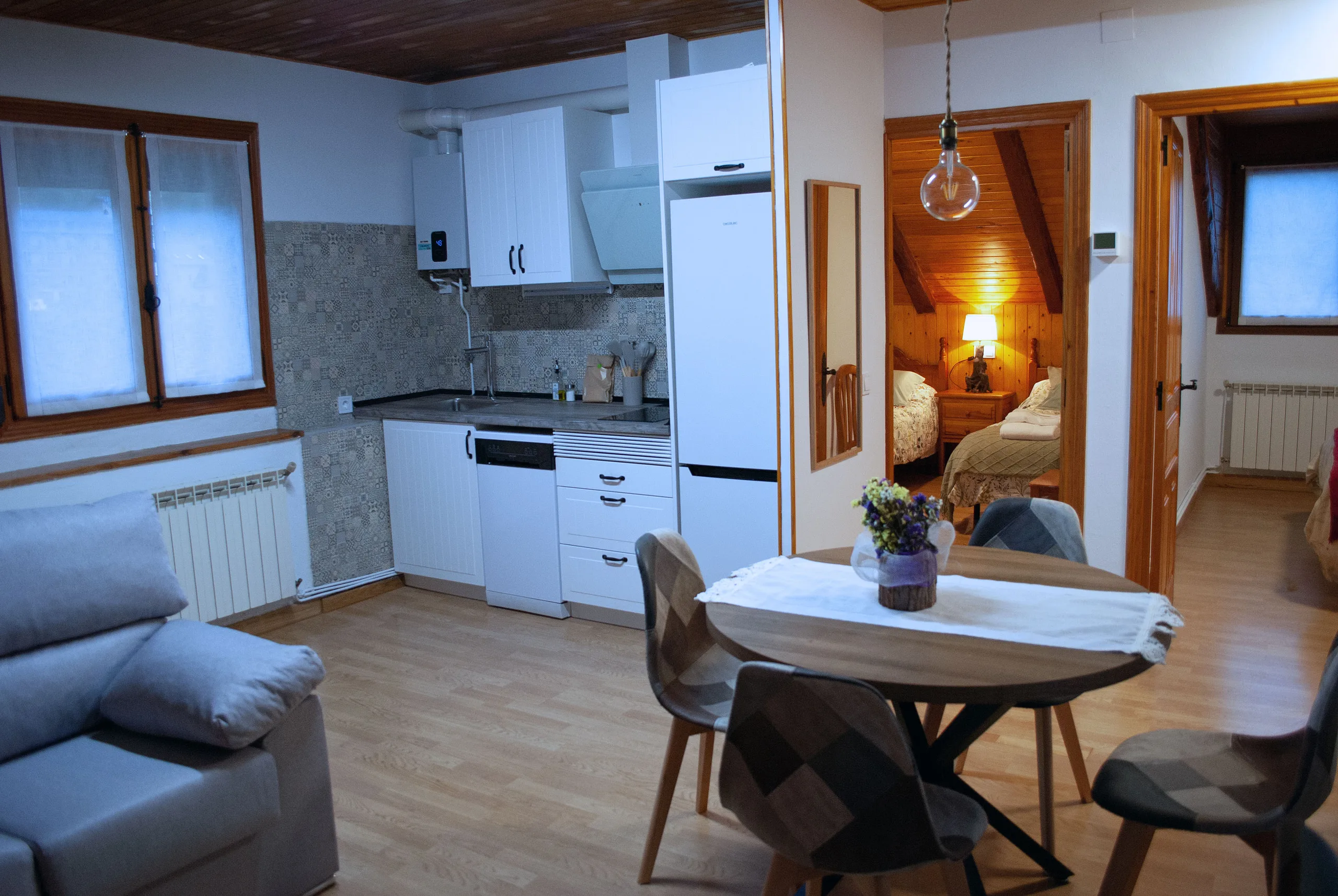 Salón-comedor con la cocina al fondo, mesa redonda para cuatro y ventanas al valle